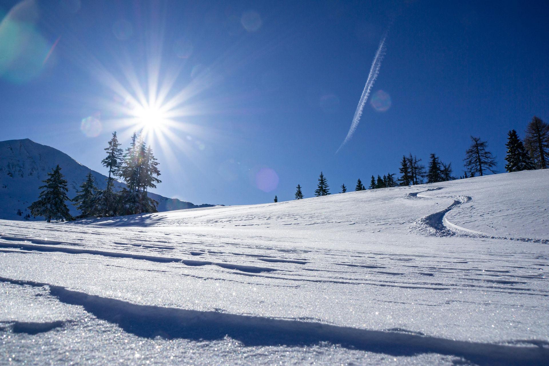 Snow-covered slope with a cross-country track and mountains in the Allgäu winter.