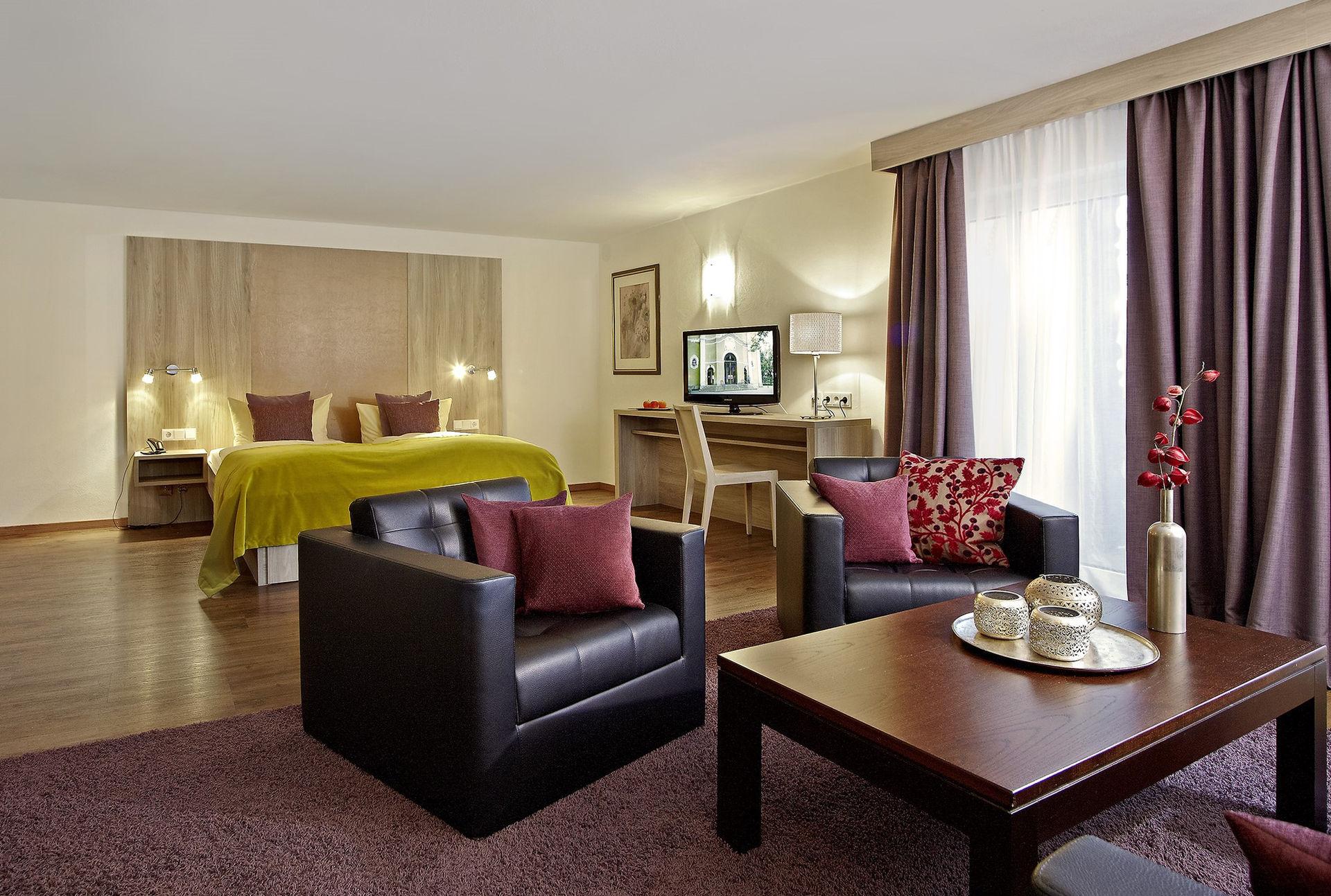 Geräumiges Hotelzimmer mit Doppelbett, Sitzbereich, Couchtisch und Schreibtisch.