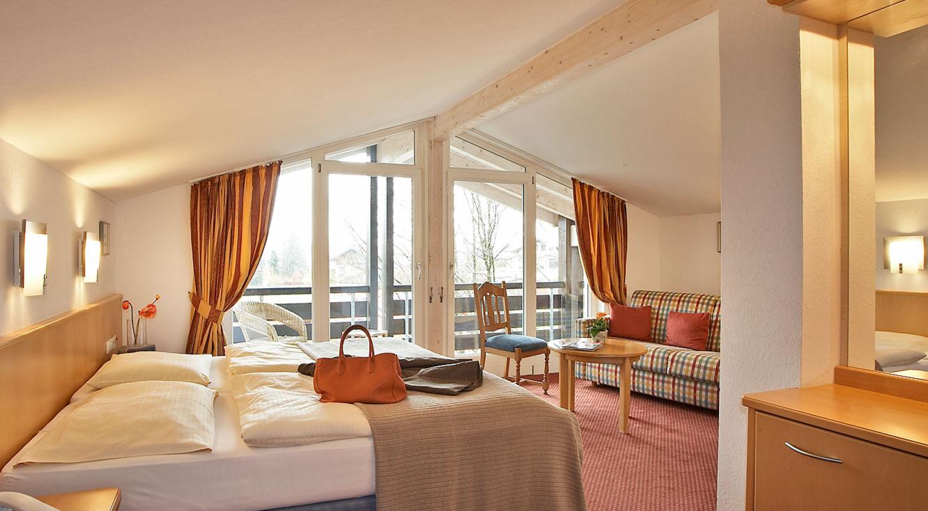 Helles Hotelzimmer mit großem Bett, Balkon und gemütlicher Sitzecke.
