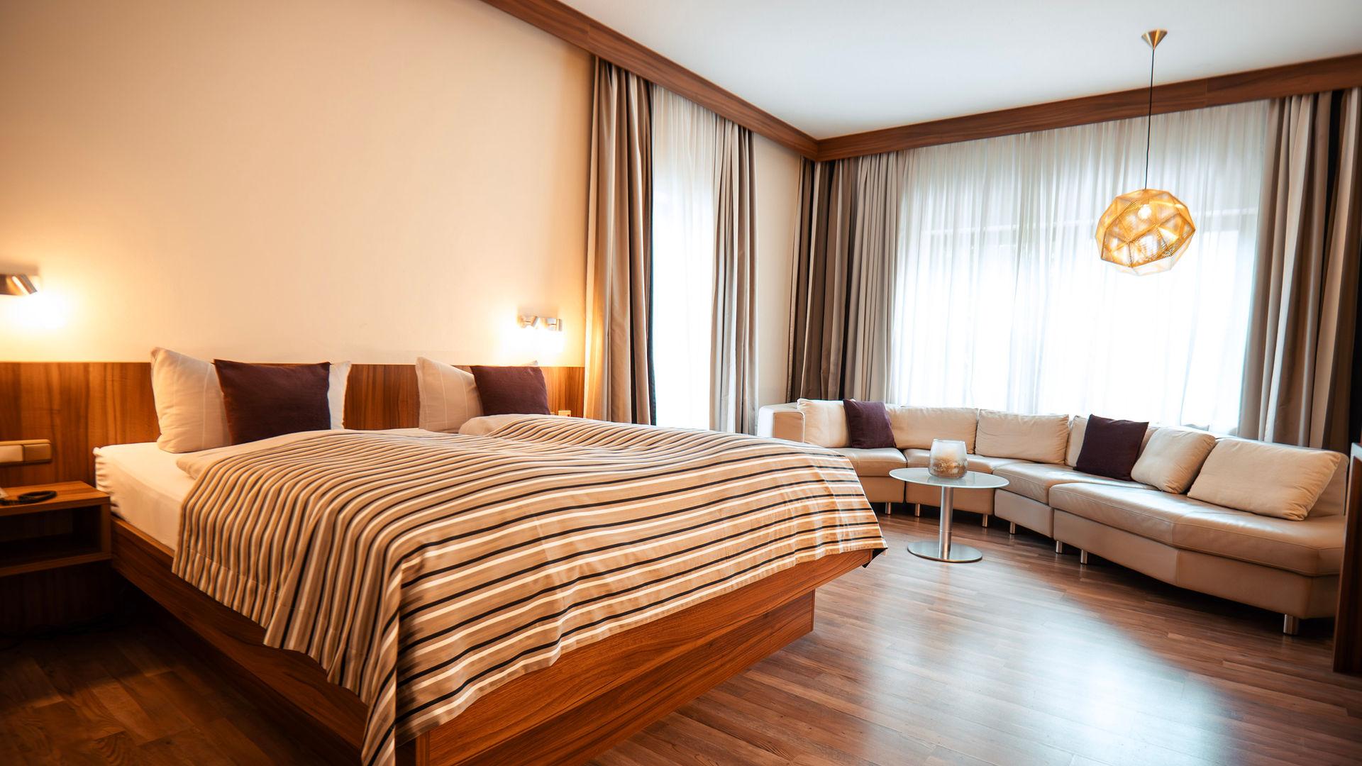 Helles, modernes Hotelzimmer mit großem Doppelbett und gemütlicher Sofalandschaft.