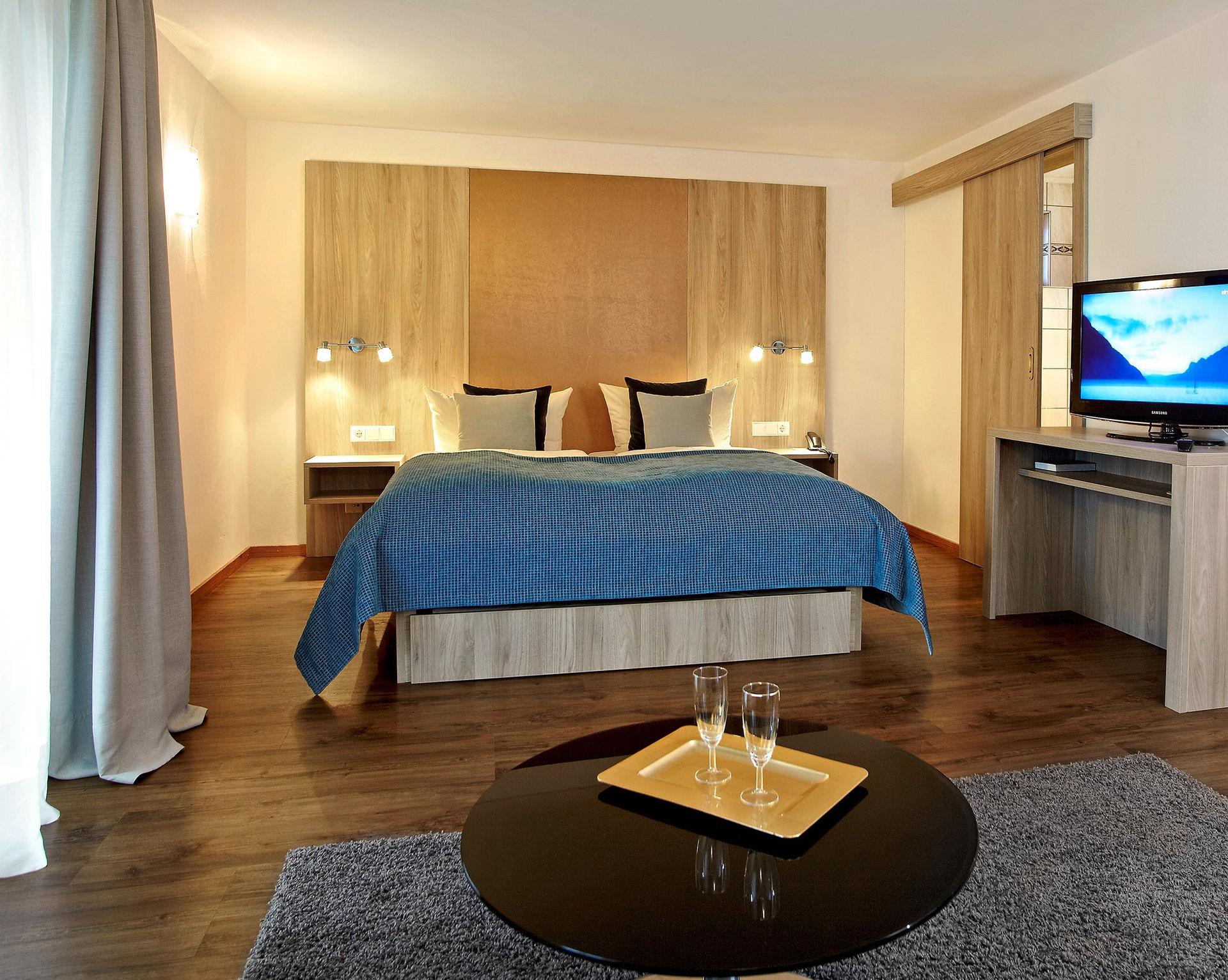 Modernes Hotelzimmer mit großem Bett, Holzkopfteil, Fernseher und Couchtisch.