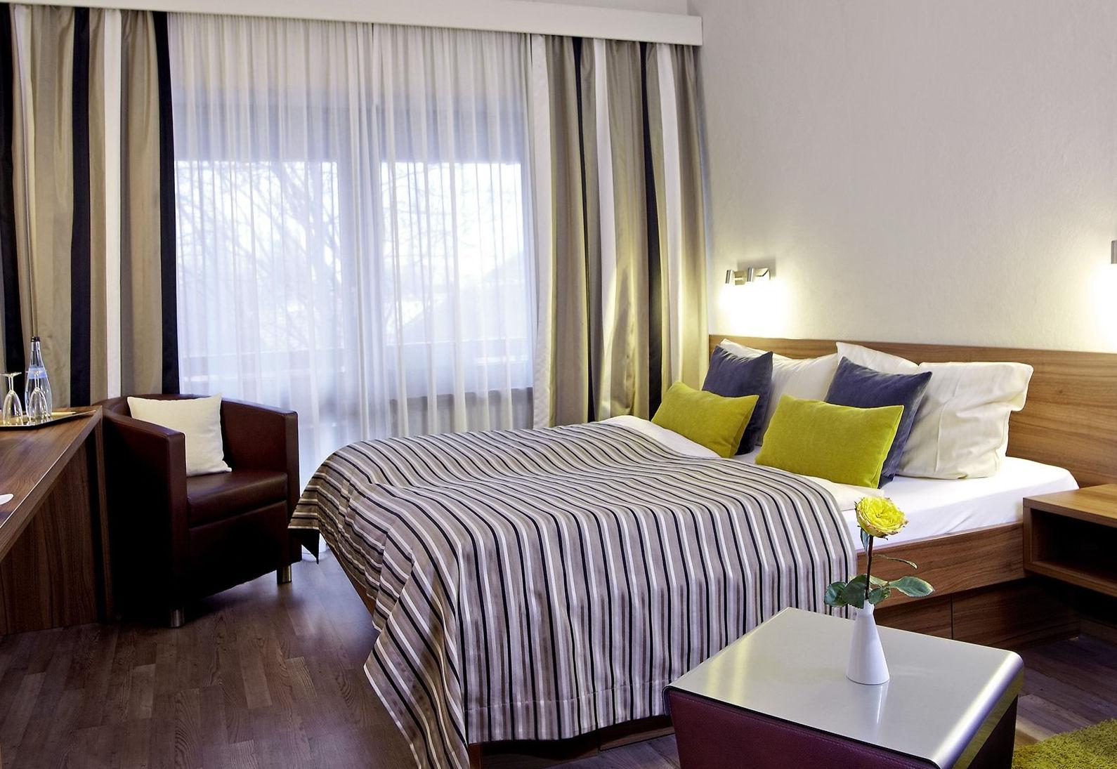 Modern hotel room with a double bed, striped bedding and a leather armchair.