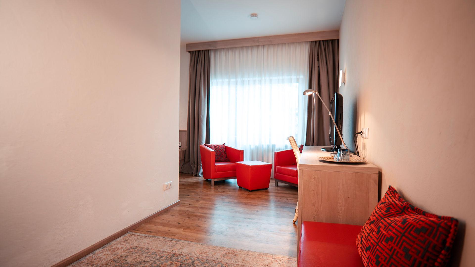 Modern hotel room with red armchairs, table, desk and window.
