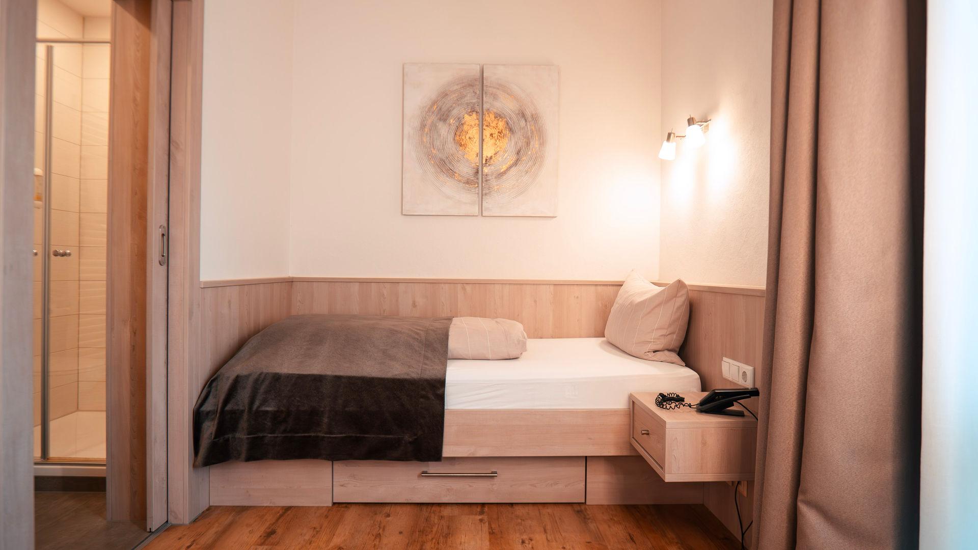 Single bed with a storage drawer, with the doorway to the bathroom and shower behind.