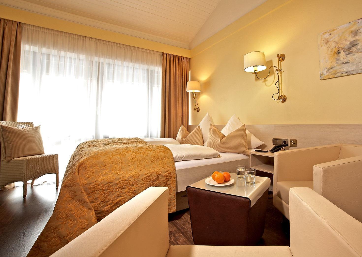 Helles, komfortables Hotelzimmer mit zwei Betten und gemütlichem Sitzbereich.