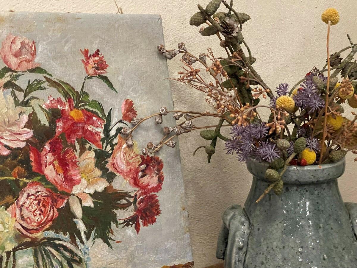 Floral still life on the wall beside dried flowers in zinc jugs.