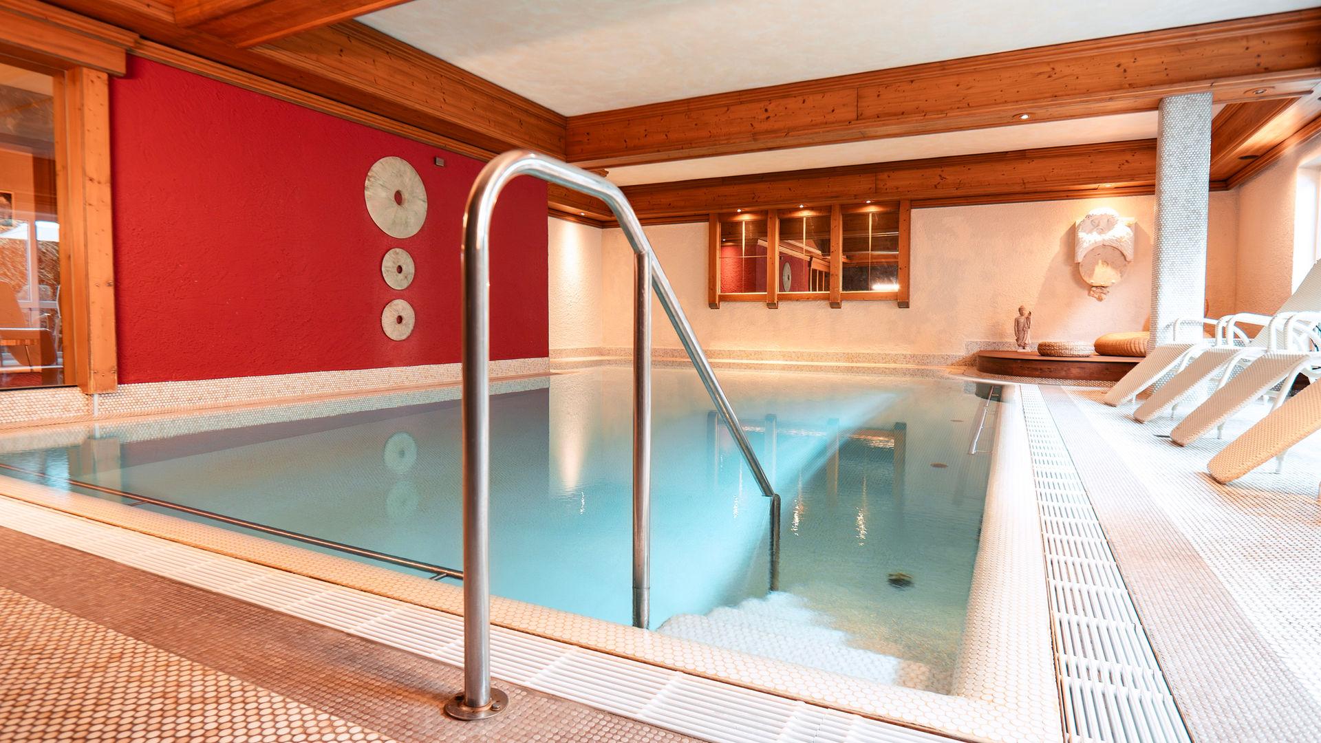 Indoor pool with turquoise water, a red wall and a wooden ceiling.