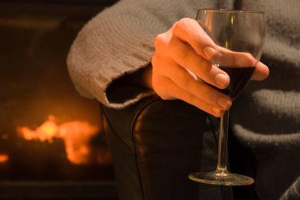 A hand holding a wine glass in front of the open fire.