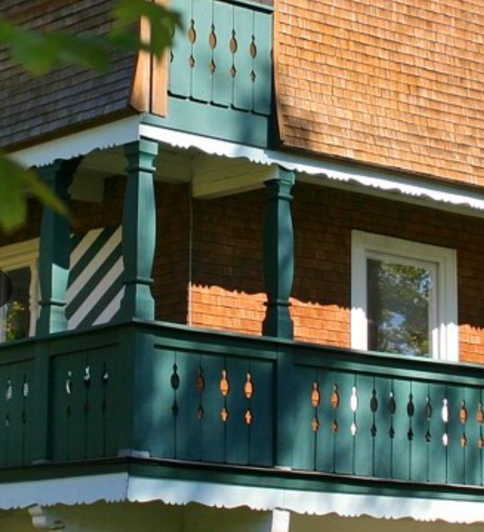 Traditioneller Balkon mit dunkelgrünem Holzgeländer im Allgäuer Sommer.