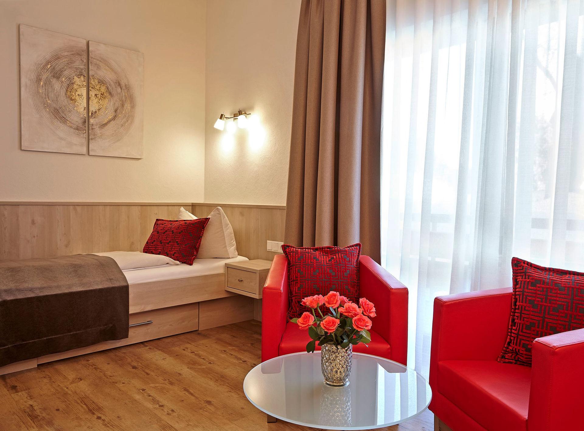 Cosy hotel room with single bed, red armchairs and flowers.