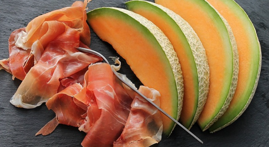 Frische Honigmelone und Parmaschinken appetitlich angerichtet auf dunklem Teller.