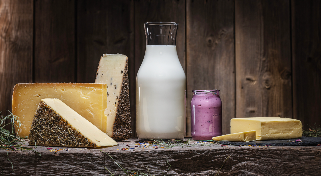 Verschiedene Käsesorten, Milchflasche und Joghurt auf rustikalem Holzhintergrund.