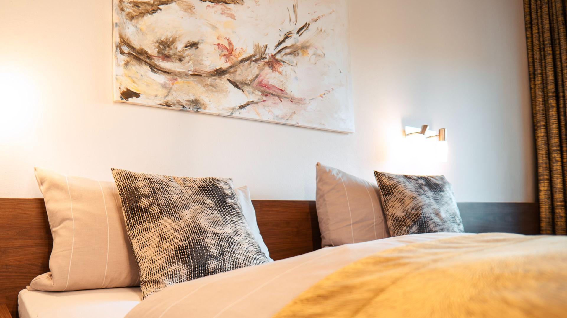 Modernes Schlafzimmer mit bequemem Bett, Kissen und abstrakter Kunst, warme Beleuchtung.